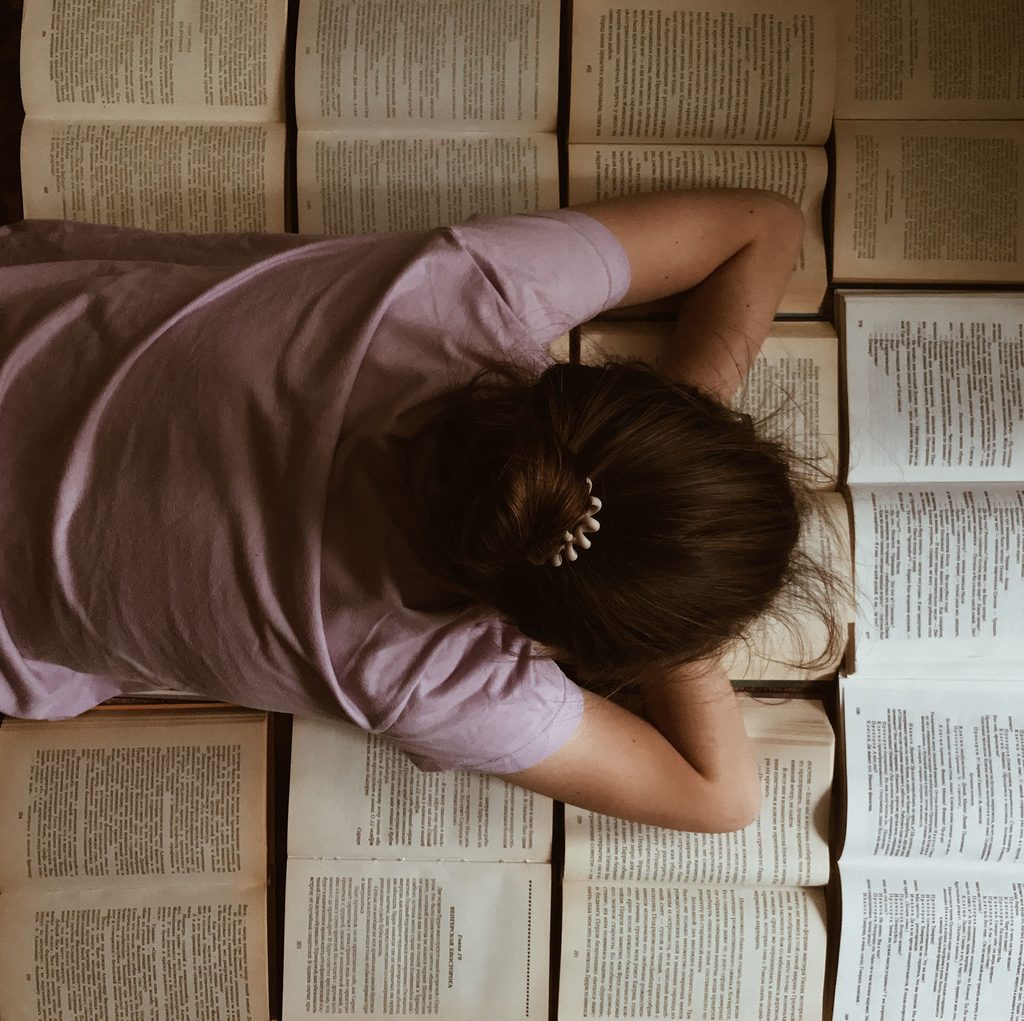Woman lying face-down among open books — 5 books I gave up on